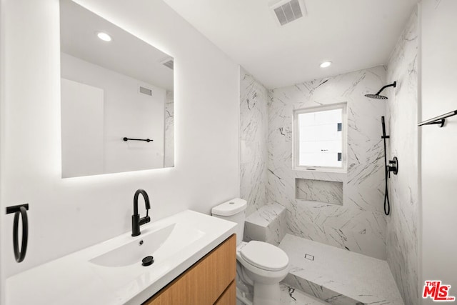 bathroom with a tile shower, vanity, and toilet