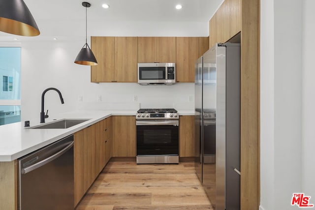 kitchen featuring sink, hanging light fixtures, stainless steel appliances, kitchen peninsula, and light wood-type flooring