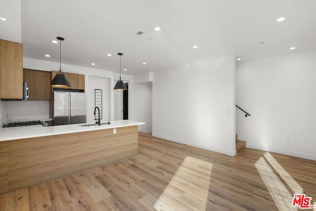 kitchen with stainless steel refrigerator, sink, light hardwood / wood-style floors, and decorative light fixtures