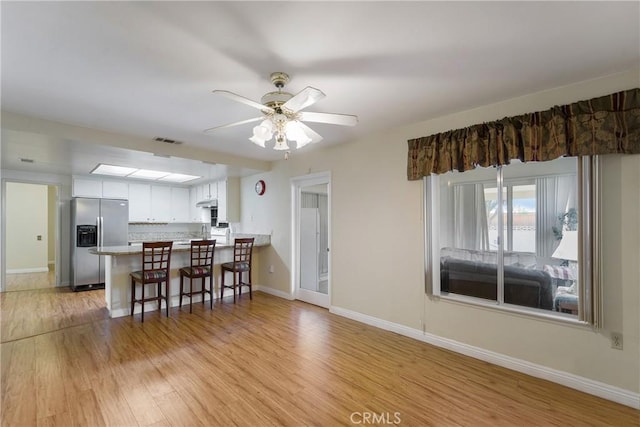 kitchen featuring kitchen peninsula, stainless steel refrigerator with ice dispenser, light wood-type flooring, ceiling fan, and white cabinets