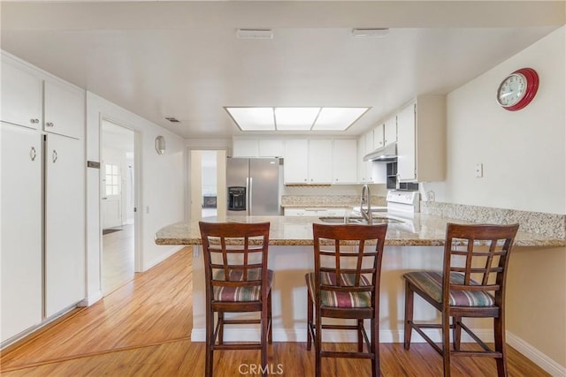 kitchen featuring white cabinetry, sink, light hardwood / wood-style flooring, kitchen peninsula, and stainless steel fridge