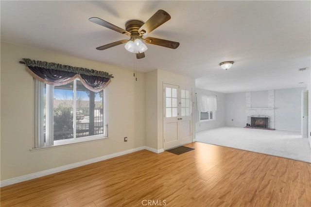 unfurnished living room featuring a large fireplace, ceiling fan, and light hardwood / wood-style flooring