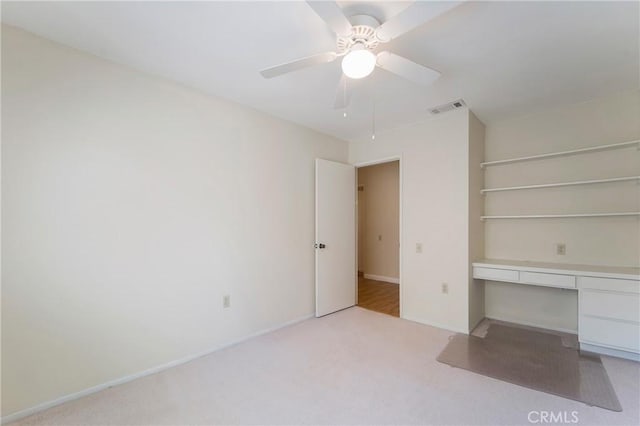 unfurnished bedroom featuring ceiling fan, built in desk, and light carpet