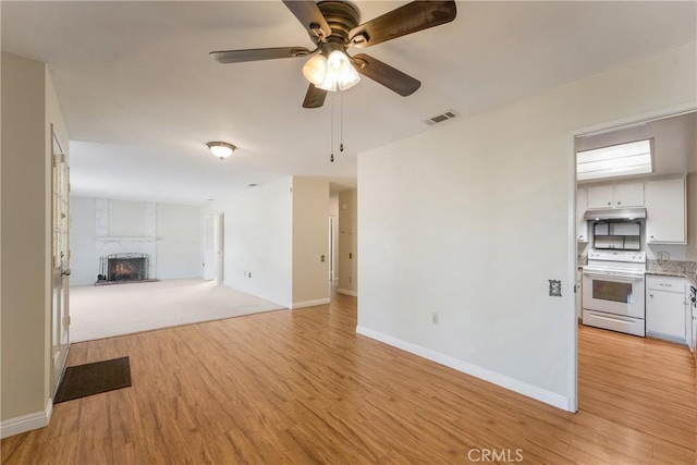 unfurnished living room featuring light wood-type flooring, a large fireplace, and ceiling fan