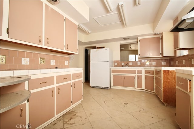 kitchen with white fridge, range hood, decorative backsplash, and light tile patterned flooring