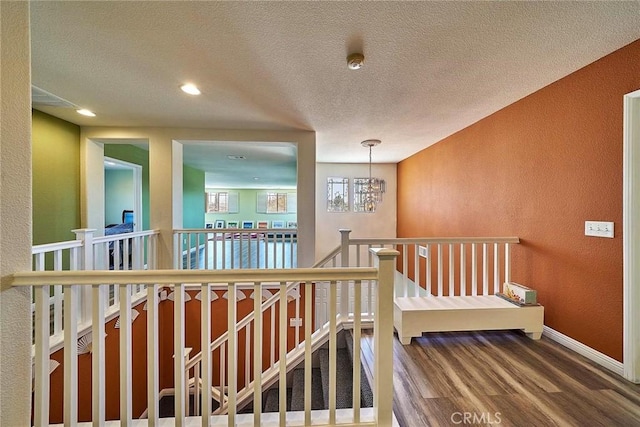 hallway with hardwood / wood-style floors, a textured ceiling, and an inviting chandelier