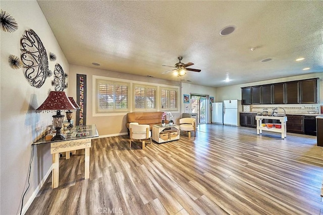 living room featuring light wood-type flooring, a textured ceiling, ceiling fan, and sink