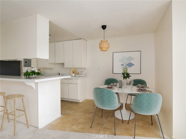 kitchen with a textured ceiling, decorative light fixtures, kitchen peninsula, and white cabinetry