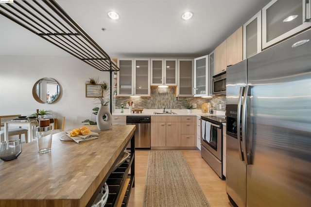 kitchen with light brown cabinets, sink, appliances with stainless steel finishes, light hardwood / wood-style floors, and tasteful backsplash