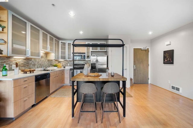 kitchen with a center island, stainless steel appliances, light wood-type flooring, and backsplash