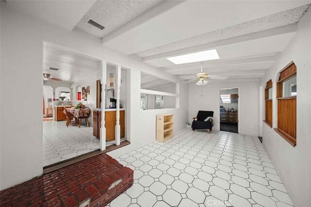 interior space with ceiling fan, lofted ceiling with beams, and a textured ceiling