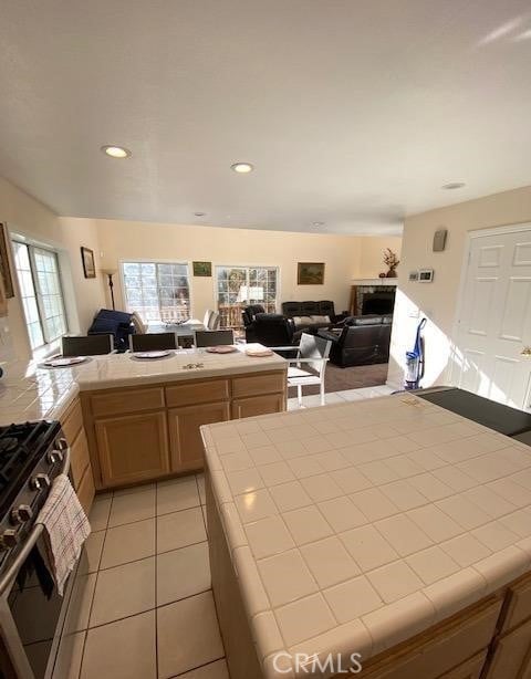 kitchen featuring light brown cabinetry, tile counters, high end stainless steel range oven, and light tile patterned floors