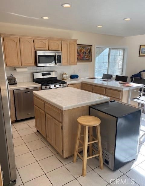 kitchen with light tile patterned floors, tasteful backsplash, stainless steel appliances, a center island, and a kitchen bar