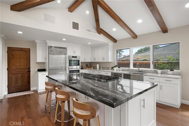 kitchen featuring dark stone counters, stainless steel appliances, sink, white cabinets, and a large island