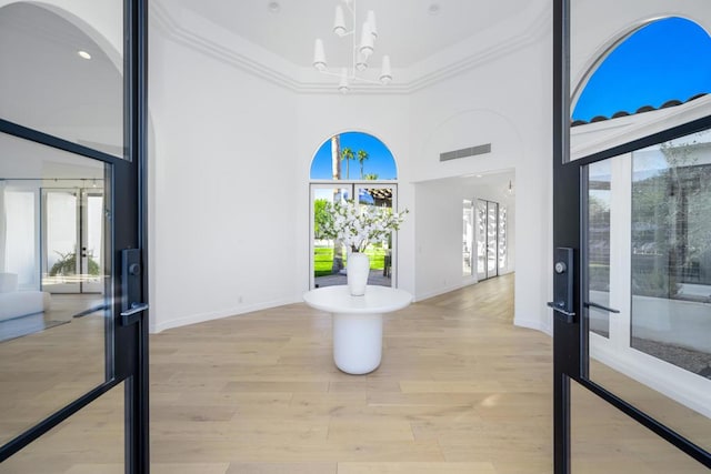 entryway with a towering ceiling, light hardwood / wood-style floors, a wealth of natural light, and ornamental molding