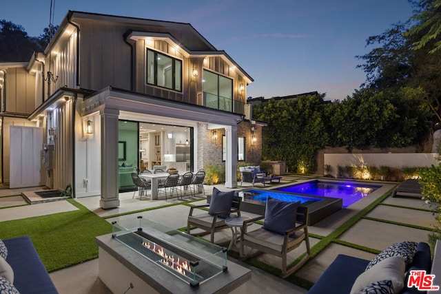 pool at dusk featuring a patio area and an outdoor living space with a fire pit