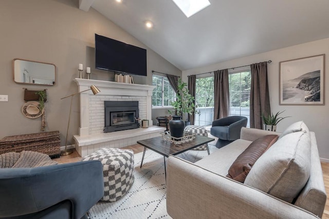 living room with vaulted ceiling with skylight, a brick fireplace, and light wood-type flooring