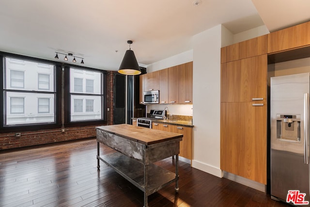 kitchen with dark hardwood / wood-style floors, dark stone countertops, track lighting, decorative light fixtures, and appliances with stainless steel finishes