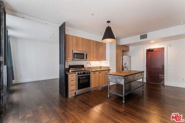 kitchen featuring sink, dark hardwood / wood-style flooring, dark stone countertops, decorative light fixtures, and appliances with stainless steel finishes