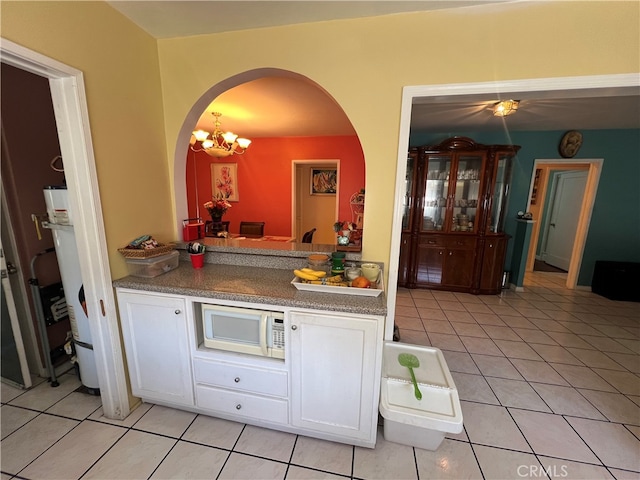 kitchen with white microwave, light tile patterned flooring, an inviting chandelier, and white cabinets