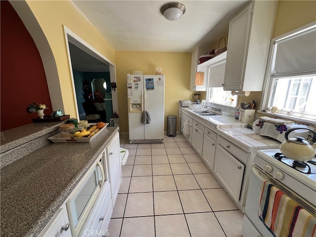 kitchen featuring sink, light tile patterned floors, white appliances, white cabinetry, and tile countertops