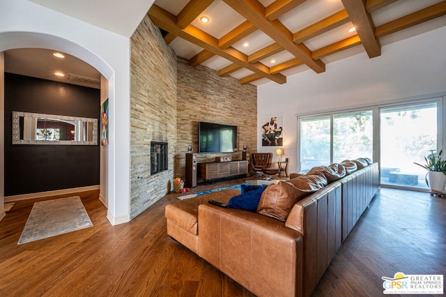 living room featuring beam ceiling, a high ceiling, coffered ceiling, a fireplace, and hardwood / wood-style flooring