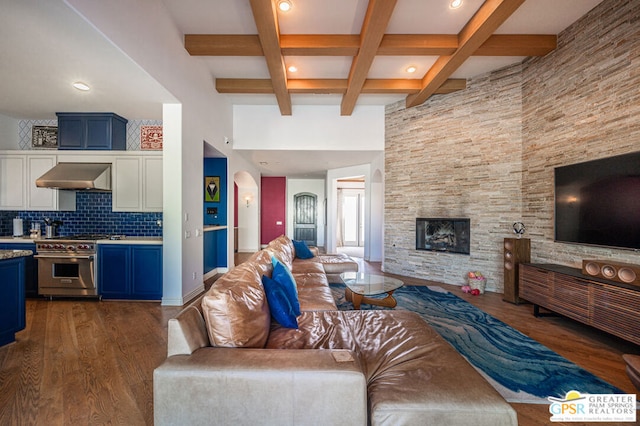 living room featuring a stone fireplace, dark hardwood / wood-style flooring, beamed ceiling, and a high ceiling