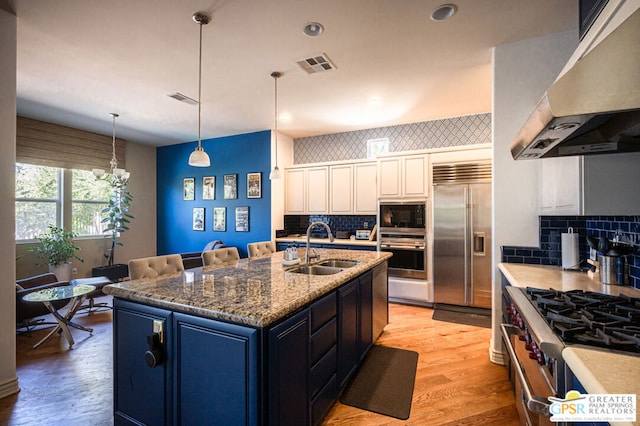 kitchen featuring sink, light hardwood / wood-style flooring, built in appliances, a center island with sink, and exhaust hood