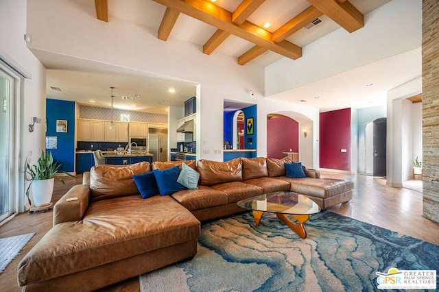 living room with beamed ceiling, a towering ceiling, and light hardwood / wood-style floors