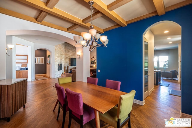 dining room featuring beam ceiling, a fireplace, a chandelier, and hardwood / wood-style flooring