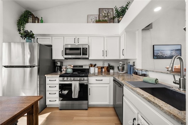 kitchen with appliances with stainless steel finishes, light stone countertops, vaulted ceiling, white cabinets, and sink