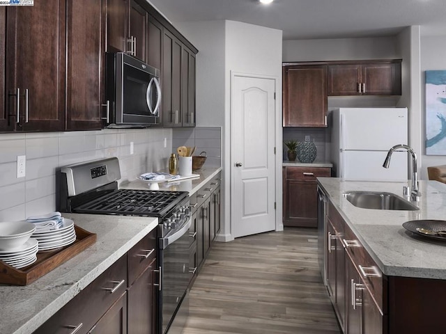 kitchen with light stone countertops, sink, stainless steel appliances, tasteful backsplash, and wood-type flooring