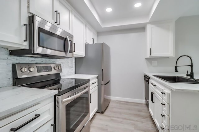 kitchen featuring sink, stainless steel appliances, a raised ceiling, light hardwood / wood-style flooring, and white cabinets