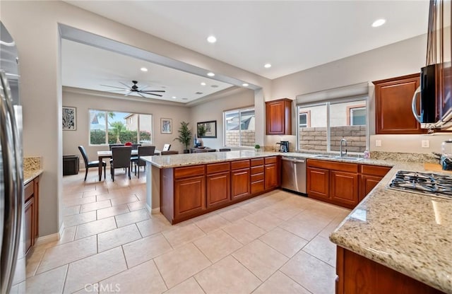 kitchen featuring kitchen peninsula, appliances with stainless steel finishes, light stone countertops, ceiling fan, and sink