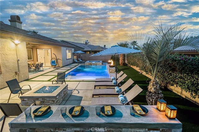 pool at dusk with pool water feature, a patio, and an outdoor fire pit