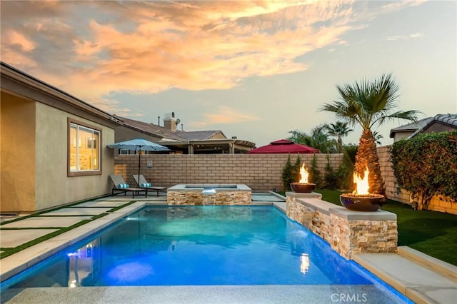 pool at dusk with an in ground hot tub, pool water feature, and an outdoor fire pit