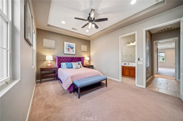 bedroom with light carpet, a tray ceiling, ensuite bath, and ceiling fan