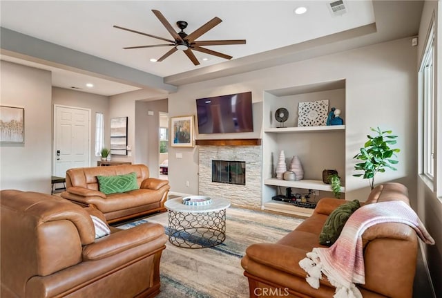 living room with a stone fireplace and ceiling fan