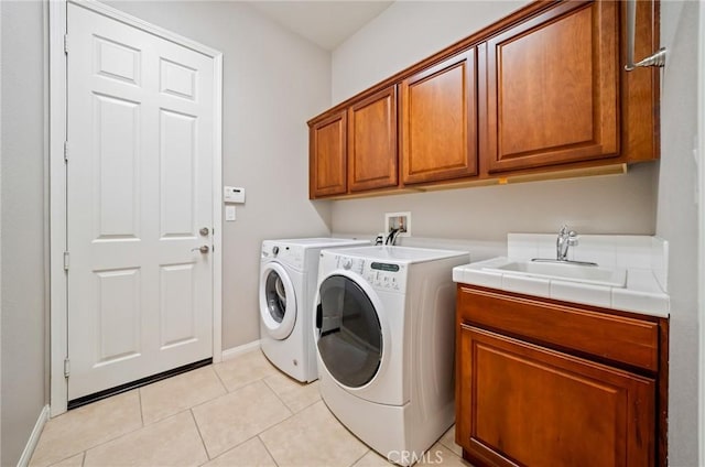 clothes washing area with washer and dryer, sink, light tile patterned floors, and cabinets