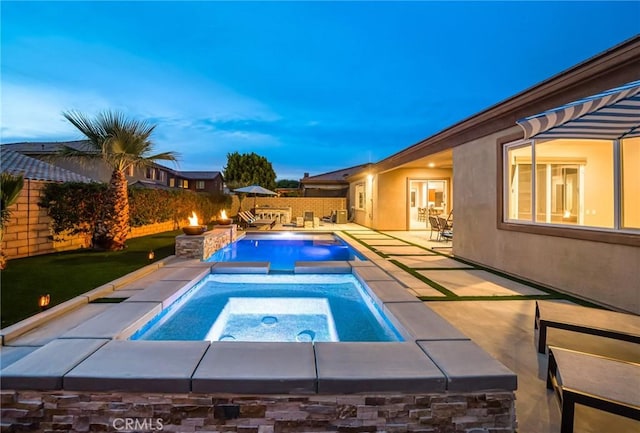 pool at dusk featuring an in ground hot tub and a patio area