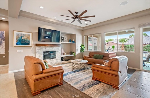 living room featuring tile patterned flooring, ceiling fan, and a stone fireplace