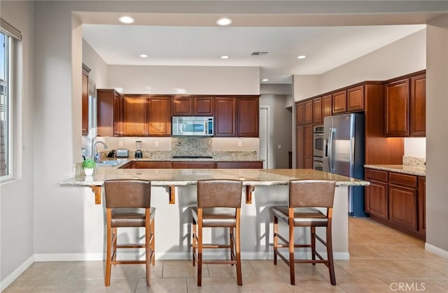 kitchen featuring light stone counters, kitchen peninsula, a kitchen bar, light tile patterned floors, and appliances with stainless steel finishes