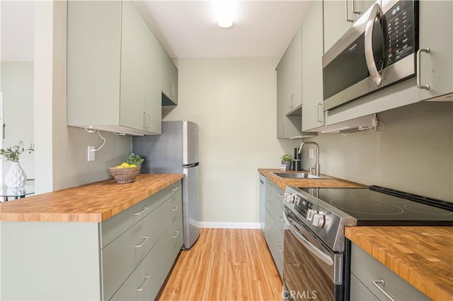 kitchen with stainless steel appliances, butcher block countertops, light hardwood / wood-style floors, and sink