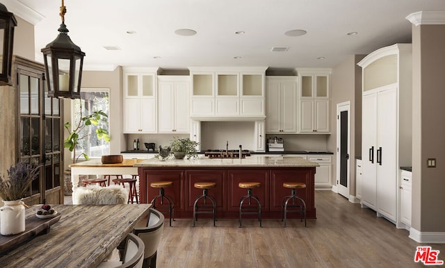 kitchen featuring light stone countertops, a kitchen bar, hardwood / wood-style floors, hanging light fixtures, and a kitchen island with sink