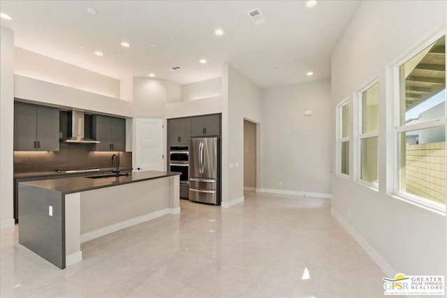 kitchen with wall chimney range hood, a breakfast bar area, appliances with stainless steel finishes, a kitchen island with sink, and sink