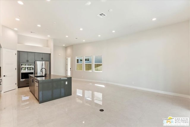 kitchen featuring light tile patterned floors, stainless steel appliances, sink, and a kitchen island with sink