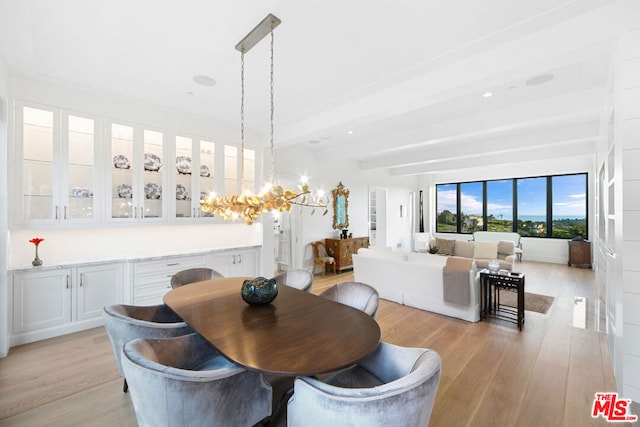 dining area with light hardwood / wood-style floors, beamed ceiling, and an inviting chandelier