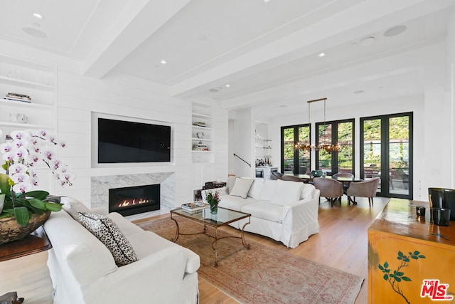 living room with built in shelves, beam ceiling, a premium fireplace, an inviting chandelier, and light hardwood / wood-style floors