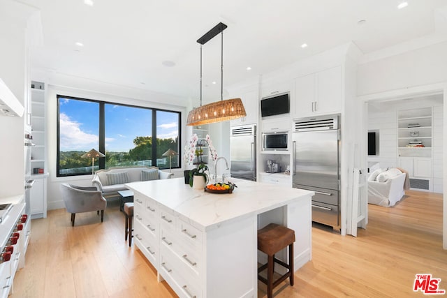 kitchen featuring light wood-type flooring, a breakfast bar, built in refrigerator, pendant lighting, and a center island with sink