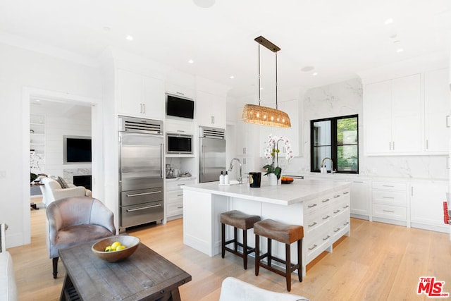 kitchen with light hardwood / wood-style floors, a kitchen island with sink, built in appliances, and white cabinetry